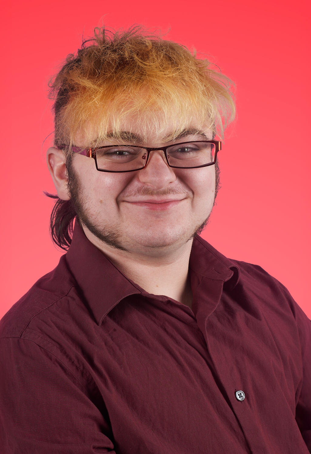Headshot of Lyle O. Lewis wearing a maroon button down on a vibrant red bacground.